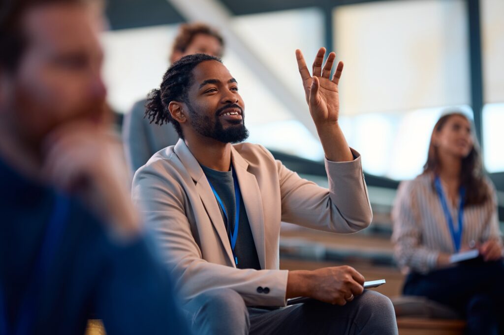 Happy black business seminar attendee asking a question from the audience.